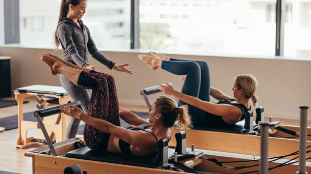 image of Women doing pilates exercises lying on pilates workout machines while their trainer guides them